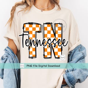 May include: Cream-colored t-shirt featuring the word "Tennessee" in a black script font, with "TN" in large orange and white checkered letters. The shirt includes the text "PNG file Digital Download".