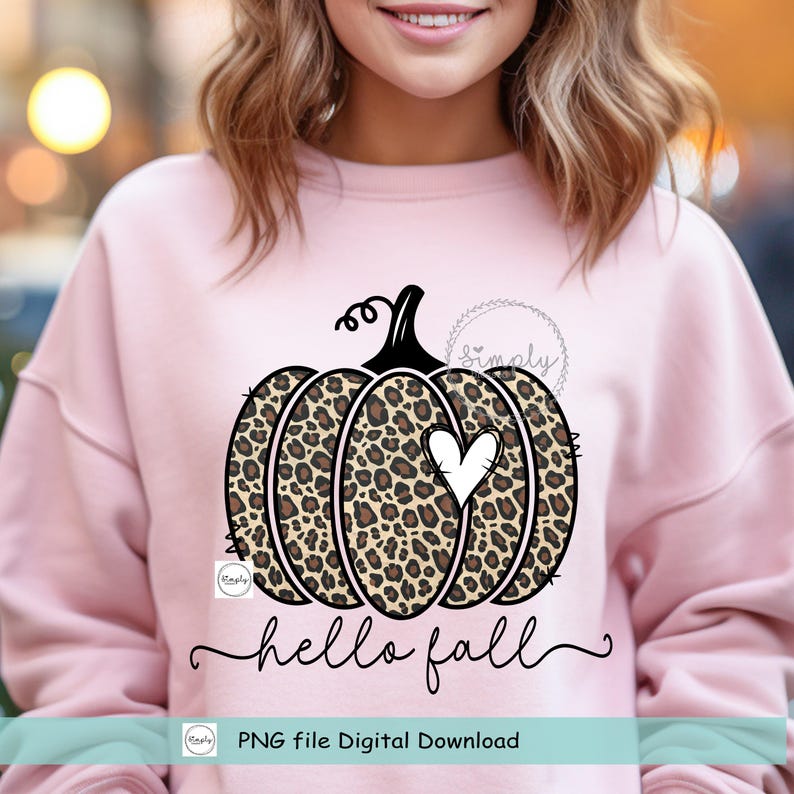 May include: A pink sweatshirt with a leopard print pumpkin with a white heart in the center. The text "hello fall" is written below the pumpkin. The text "PNG file Digital Download" is written at the bottom of the image.