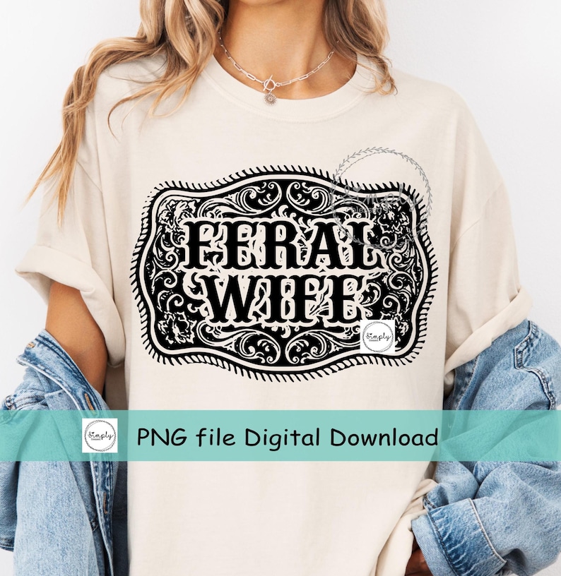 May include: A white t-shirt with a black and white graphic of a belt buckle with the text "Feral Wife" inside. The graphic is surrounded by a decorative floral design.