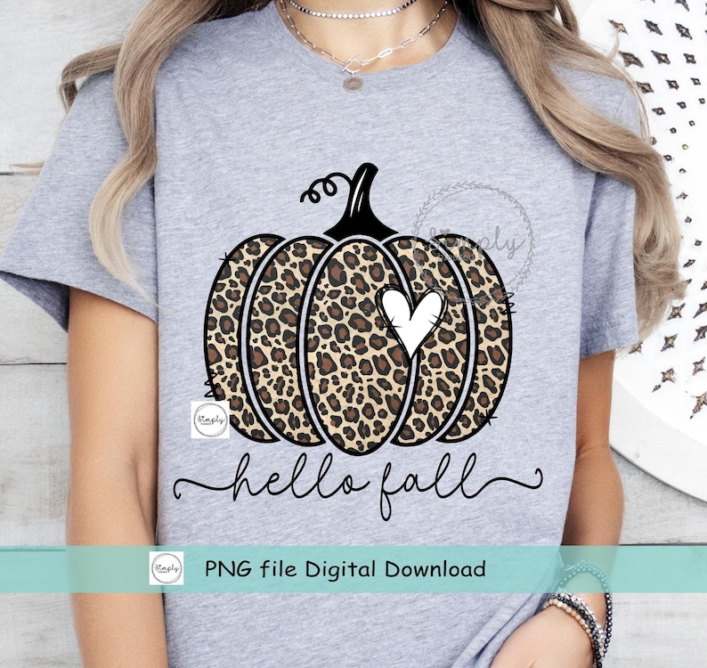 May include: A gray t-shirt with a black and brown leopard print pumpkin with a white heart in the center. The text "hello fall" is written in black cursive below the pumpkin. The text "PNG file Digital Download" is written in black below the text "hello fall".