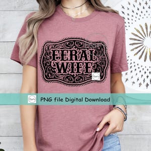 May include: A pink t-shirt with a black and white graphic of a belt buckle with the text "FERRAL WIFE" inside.