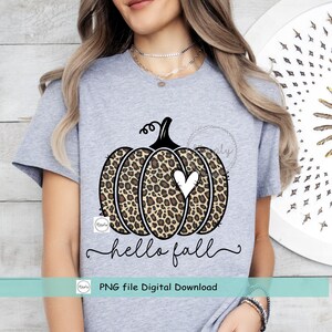 May include: A gray t-shirt with a black and brown leopard print pumpkin with a white heart in the center. The text "hello fall" is written in black cursive below the pumpkin. The text "PNG file Digital Download" is written in black below the text "hello fall".