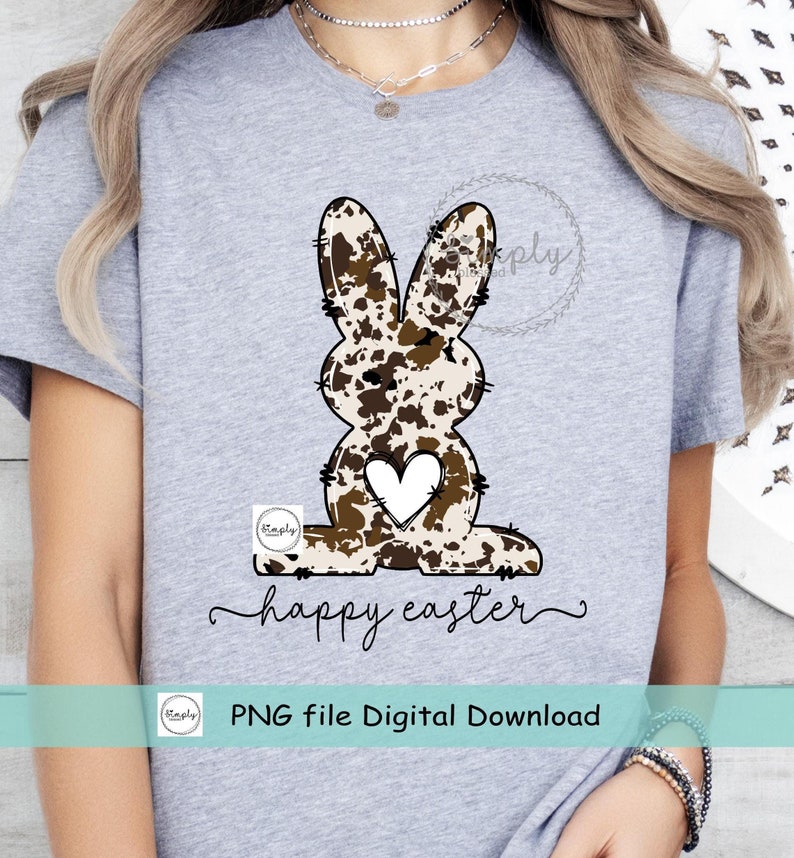 May include: A digital download of a graphic design featuring a brown and white cow print bunny with a white heart on its chest. The bunny is sitting down and the text "happy easter" is written below it. The text "PNG file Digital Download" is written below the bunny.