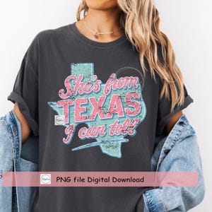 Puede incluir: Camiseta gris oscuro con el texto "She's from TEXAS I can tell" en rosa y azul, con un gr&aacute;fico del contorno de Texas. La camiseta es una descarga digital.