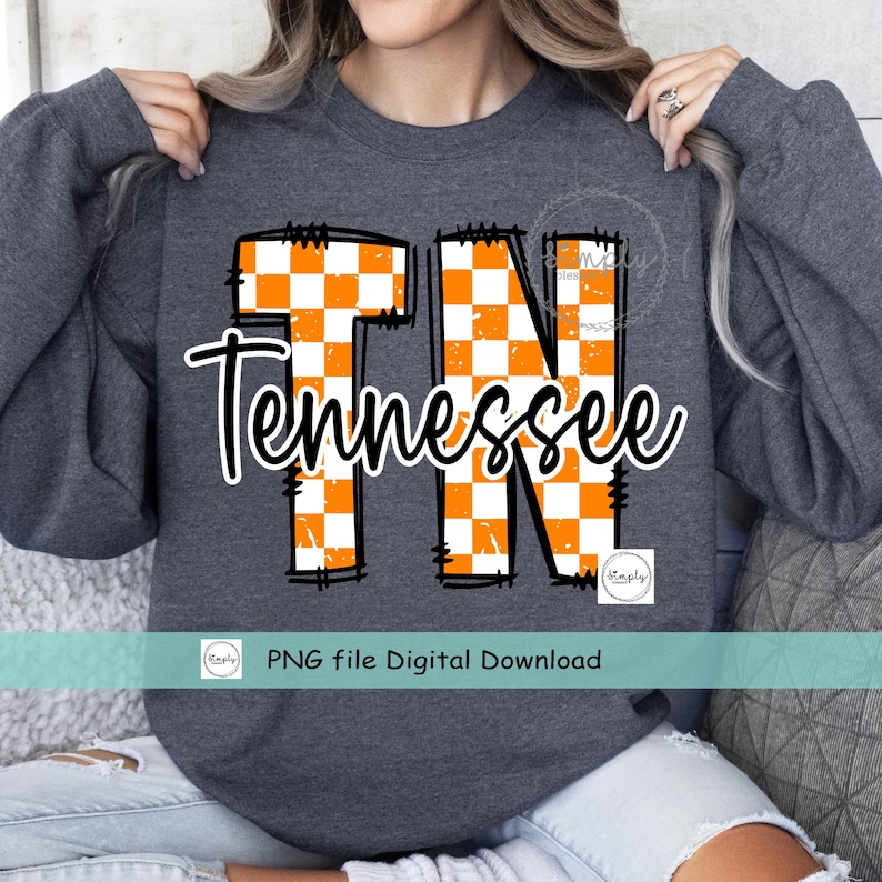 May include: Dark gray sweatshirt featuring the word "Tennessee" in a cursive font, with "TN" in large, orange and white checkered letters. The sweatshirt has long sleeves and a crew neck.