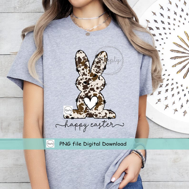 May include: A gray t-shirt with a brown and white cow print bunny with a heart in the center. The text "happy easter" is written below the bunny. The text "PNG file Digital Download" is written below the text.