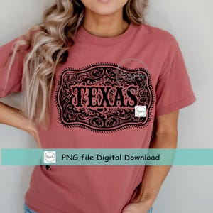 May include: A dusty rose-colored t-shirt featuring a black graphic of a decorative belt buckle with the word "TEXAS" in bold letters. The buckle design includes intricate scrollwork. The shirt also has the text "PNG file Digital Download".