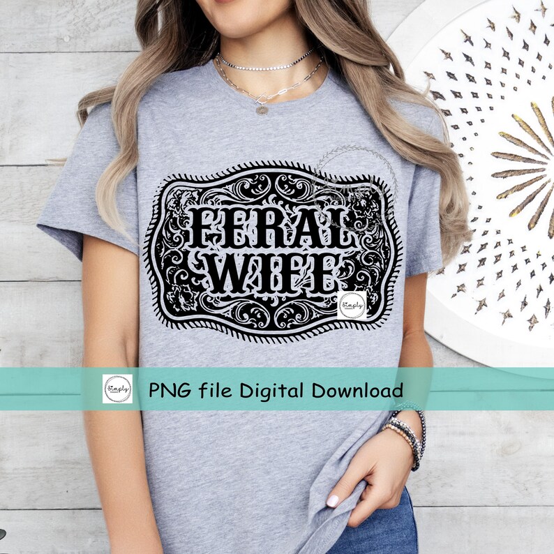 May include: A gray t-shirt with a black and white graphic of a belt buckle with the text "Feral Wife" inside.