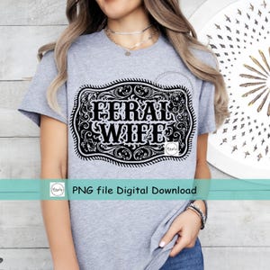 May include: A gray t-shirt with a black and white graphic of a belt buckle with the text "Feral Wife" inside.