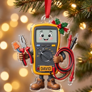 May include: A flat, hanging Christmas ornament shaped like a yellow digital multimeter with a cartoon face. The character holds pliers and test leads, wears brown boots, and features the name DAVID printed on the front with a holly sprig accent.