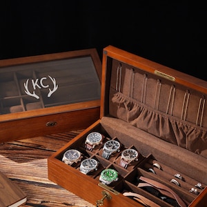 Könnte beinhalten: Eine hölzerne Uhren- und Schmuckaufbewahrungsbox mit Klappdeckel, braunem Samtinnenfutter, mehreren Uhrenfächern, Ringhaltern und einem Schloss. Eine zweite passende Box mit Glasdeckel zeigt die eingravierten Initialen KC.