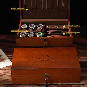 May include: A wooden jewellery box with compartments for watches, rings, and necklaces. The box is open, revealing several watches and rings. The lid of the box is closed, with the initials "C.D.A" engraved on the top.