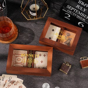 May include: Two rectangular wooden boxes with glass lids containing playing cards and dice. One box is labeled "BENNETT" and the other "Madeline POKER SET". The set includes loose playing cards, two small textured lighters, and circular poker chips.