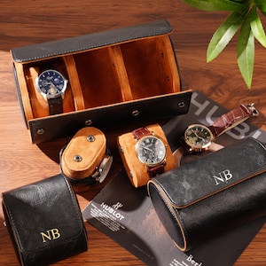 May include: An assortment of luxury watches and watch cases. The watches have leather bands and gold or silver watch faces. The watch cases are black leather with the initials "NB" and a three-watch travel case.
