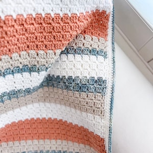 May include: A crocheted blanket with stripes of white, beige, light blue, and peach.
