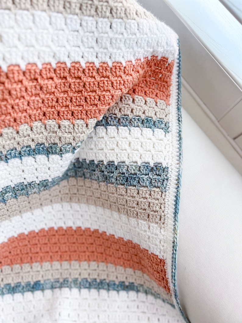 May include: A crocheted blanket with stripes of white, beige, light blue, and peach.