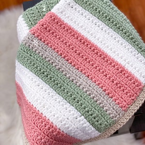 Op de afbeelding: Een gestreept gebreid babydekentje in de kleuren roze, groen, wit en grijs.