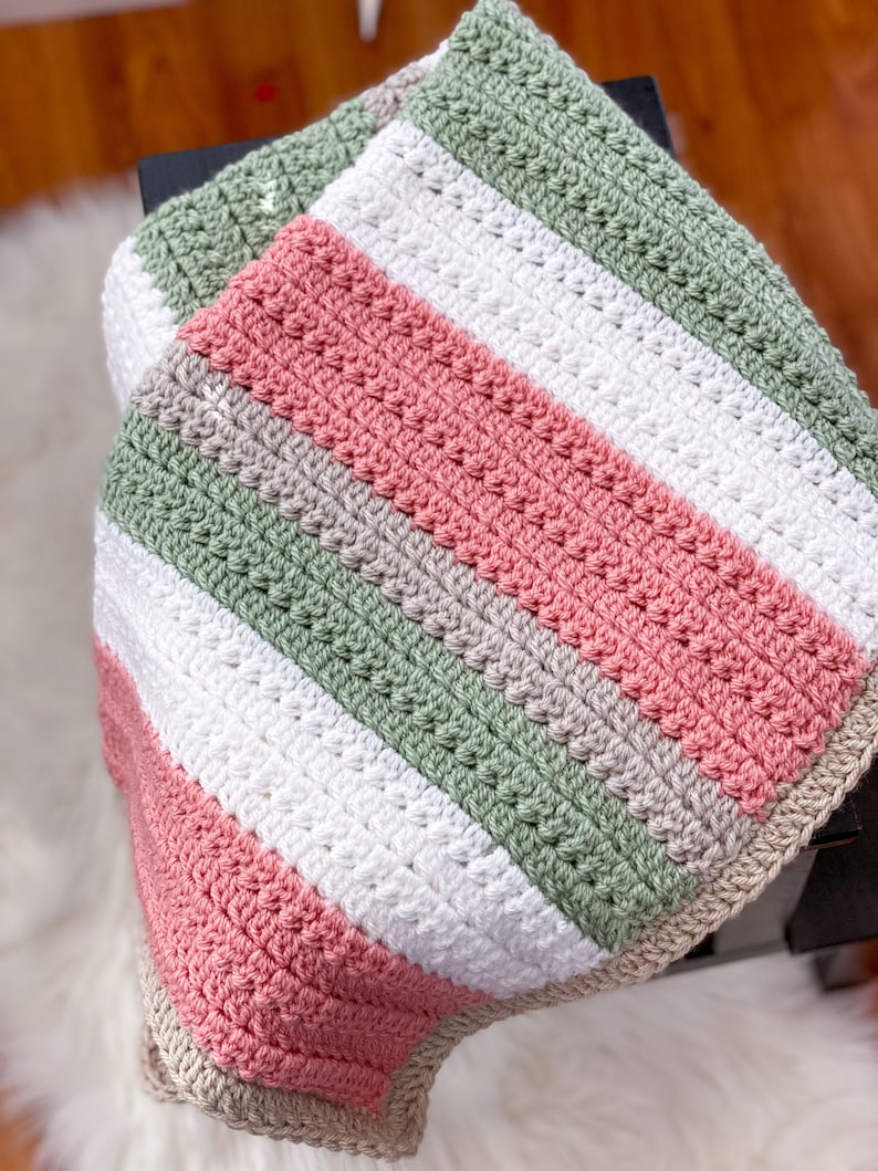 Op de afbeelding: Een gestreept gebreid babydekentje in de kleuren roze, groen, wit en grijs.