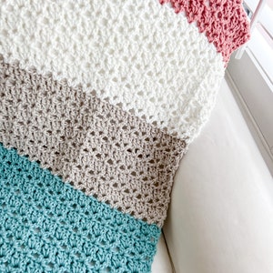 Pu&ograve; includere: Una coperta all'uncinetto con strisce turchesi, beige, bianche e rosa.