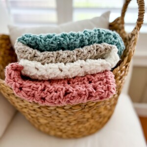 Pu&ograve; includere: Un cesto di vimini pieno di quattro coperte all'uncinetto in tonalit&agrave; rosa, bianco, beige e turchese.