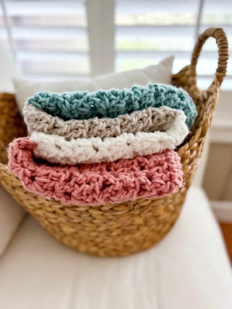 Pu&ograve; includere: Un cesto di vimini pieno di quattro coperte all'uncinetto in tonalit&agrave; rosa, bianco, beige e turchese.