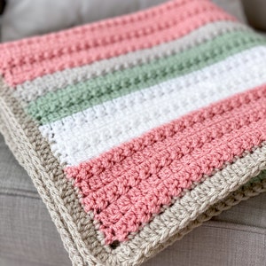 Op de afbeelding: Een gehaakt babydekentje met strepen in roze, groen, wit en beige.
