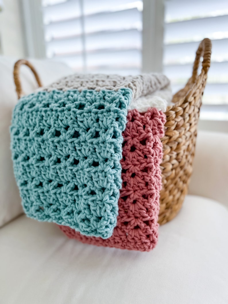 Pu&ograve; includere: Un cesto di vimini pieno di coperte all'uncinetto in turchese, rosa e beige. Le coperte sono piegate e impilate nel cesto.