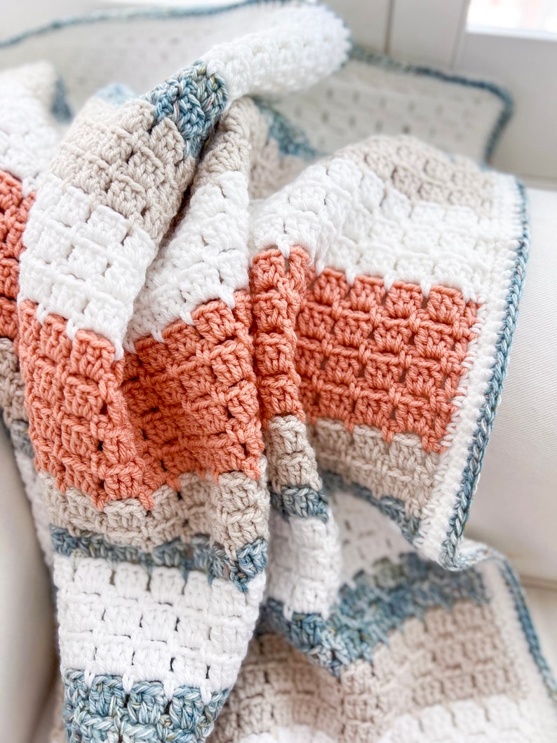 May include: A crocheted blanket with stripes of white, beige, light blue, and peach.