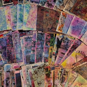 May include: A large collection of rectangular paper sheets featuring mixed media art with vibrant watercolor splashes, ink splatters, and printed text fragments in various colors including pink, blue, yellow, and brown, arranged in a fan-like pattern.