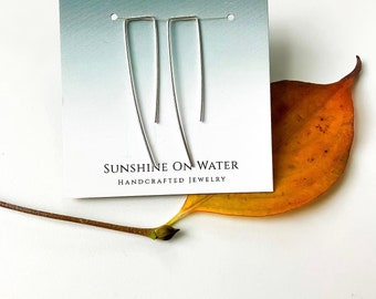 May include: A pair of silver earrings with a simple, geometric design. The earrings are displayed on a white card with the text "Sunshine on Water Handcrafted Jewelry".