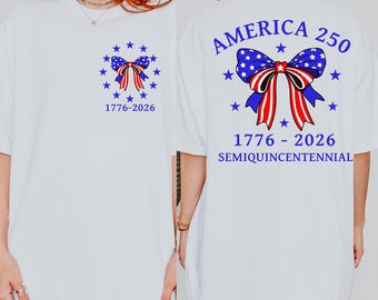 May include: White t-shirt featuring a patriotic design. The front displays a blue bow with red stripes and stars, surrounded by stars, and the text "1776-2026." The back of the shirt reads "AMERICA 250" above a similar bow design, with "1776-2026 SEMIQUICENTENNIAL" below.