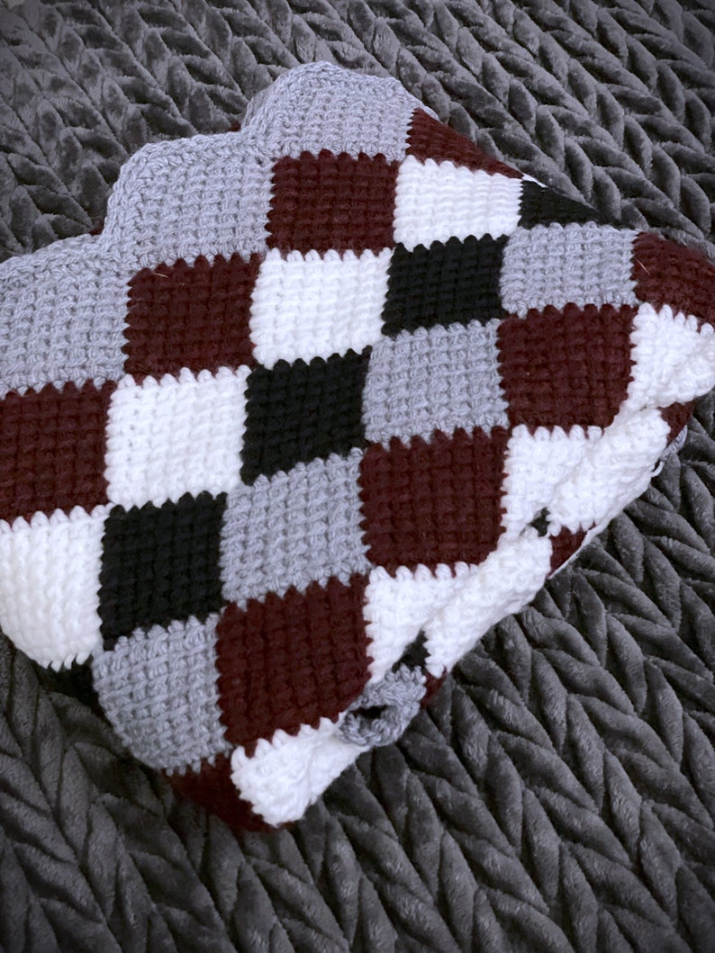 May include: A crocheted blanket with a checkered pattern in burgundy, white, black, and gray.
