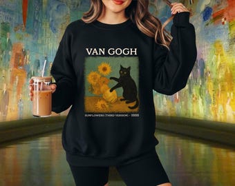 May include: Black sweatshirt featuring a graphic of Van Gogh's "Sunflowers" with a black cat. The design includes the text "VAN GOGH" above the image and "SUNFLOWERS (THIRD VERSION) - 1888" below. The sweatshirt is black.
