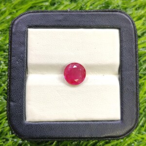 Könnte beinhalten: Ein facettierter, runder, leuchtend roter Edelstein, wahrscheinlich ein Rubin, liegt in einer schwarz-weißen Präsentationsbox. Die polierte Oberfläche des Steins reflektiert das Licht und zeigt seine Klarheit und Farbe. Die Box hebt den Glanz des Edelsteins hervor.
