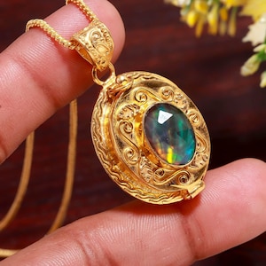 May include: A gold pendant necklace featuring an oval, iridescent gemstone. The pendant has an ornate, filigree design. The chain is also gold. The gemstone is set in a gold-colored, decorative setting.