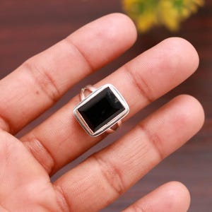 Peut inclure: Bague en argent ornée d'une pierre noire rectangulaire. La bague présente un design simple et élégant avec un anneau en argent poli et un sertissage à lunette. La forme rectangulaire de la pierre est mise en valeur.