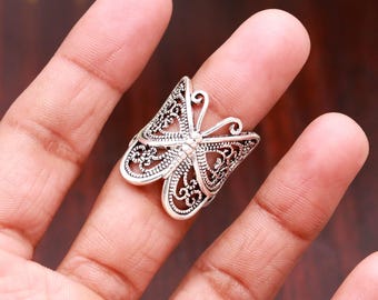 May include: A silver-toned ring featuring a butterfly design with intricate filigree cutouts. The metal surface has a darkened, oxidized finish within the recessed areas of the wings, highlighting the detailed scrollwork patterns throughout.