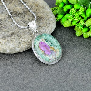 Peut inclure: Un collier en argent avec un pendentif ovale. Le pendentif présente une pierre aux teintes vertes, roses et dorées. La pierre est sertie dans un cadre argenté et suspendue à une chaîne en argent. Un bijou.