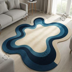 Könnte beinhalten: Ein abstrakt geformter Teppich mit cremefarbenem Mittelteil und geschichteten blauen wellenförmigen Rändern. Das Design des Teppichs weist Marine-, Mittel- und Hellblautöne auf und erzeugt einen modernen und künstlerischen Look. Der Teppich liegt auf einem hellen Holzboden.