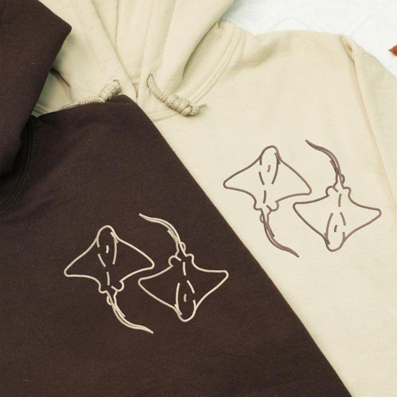 Puede incluir: Se muestran dos sudaderas con capucha, una marr&oacute;n oscuro y otra beige. Cada sudadera con capucha presenta un dise&ntilde;o a juego de dos rayas en un estilo minimalista. Las sudaderas con capucha tienen cordones y una capucha. El dise&ntilde;o de la raya es de un color contrastante.