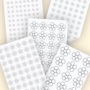 May include: Several white sheets of paper with black floral designs. The sheets are arranged at different angles, displaying various sizes and arrangements of the flower patterns. Some sheets have the number "05" or "15" printed on them.