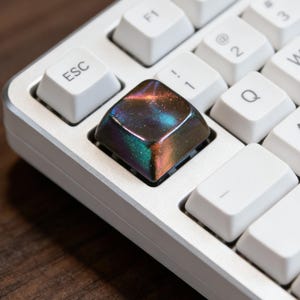 May include: A trio of ceramic mugs with a speckled, matte finish in cream, light grey, and dark grey. Each mug features a simple, minimalist design, ideal for tea or coffee.