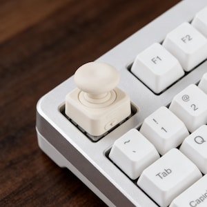 May include: A white ceramic mug with a black handle and the text "But First, Coffee" in a black, handwritten-style font. The mug is on a white surface.