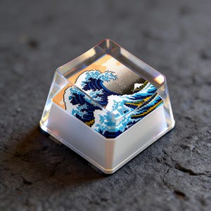 May include: A clear, square keycap featuring a pixelated image of Hokusai's Great Wave off Kanagawa. The keycap has a white base and a transparent top, showcasing the artwork. The wave is depicted in shades of blue, white, and yellow.