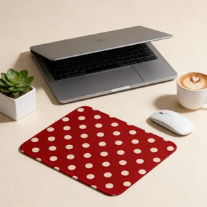 May include: A red mousepad with white polka dots sits on a desk next to a laptop, a white mouse, a cup of coffee, and a small succulent plant in a white square pot.