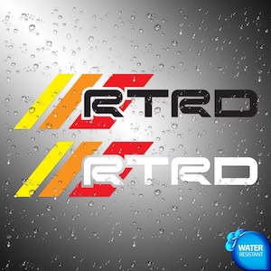 Op de afbeelding: Twee grafische stickers met de tekst RTRD in een gestileerd lettertype, één in zwart en één in wit. Elke tekst wordt voorafgegaan door drie diagonale strepen in geel, oranje en rood. De achtergrond is een donkergrijs verloop met waterdruppels.