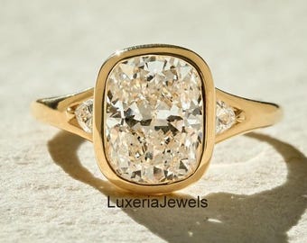 May include: A gold ring with a large, rectangular, light-colored gemstone. The gemstone is surrounded by a gold bezel setting. Two smaller triangular gemstones flank the main stone. The ring is on a neutral surface. The text "LuxeriaJewels" is visible.
