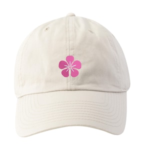 May include: A cream-colored baseball cap featuring a pink flower graphic on the front. The cap has a curved brim and an adjustable strap at the back. The flower design is a simple, five-petal blossom with a white center.