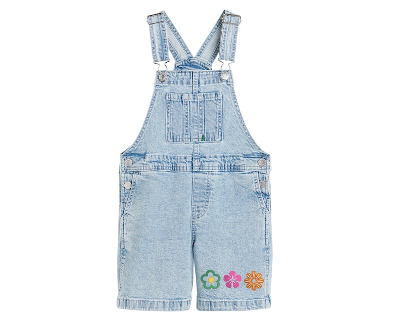 May include: Light blue denim overall shorts with adjustable straps and a front bib pocket. The shorts feature three embroidered flowers in green, pink, and orange near the hem. The garment is made of a light wash denim.