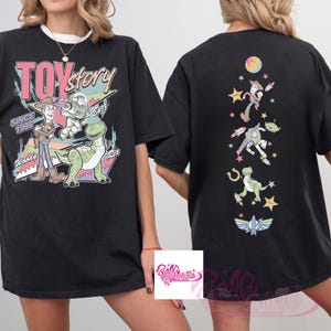 May include: Black t-shirt featuring Toy Story characters. The front graphic includes Woody, Buzz Lightyear, Rex, and the text "TOY STORY SINCE 1995". The back of the shirt has a vertical design with various characters and a moon.